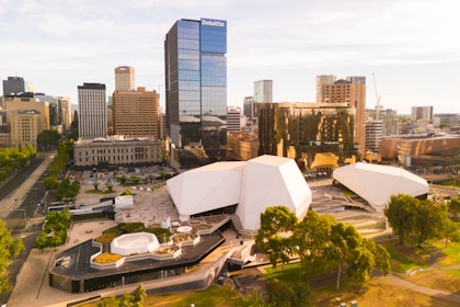 Adelaide cityscape with Adelaide Festival Centre's white shell-like roofs, a river, bridge, and city skyline in the background.